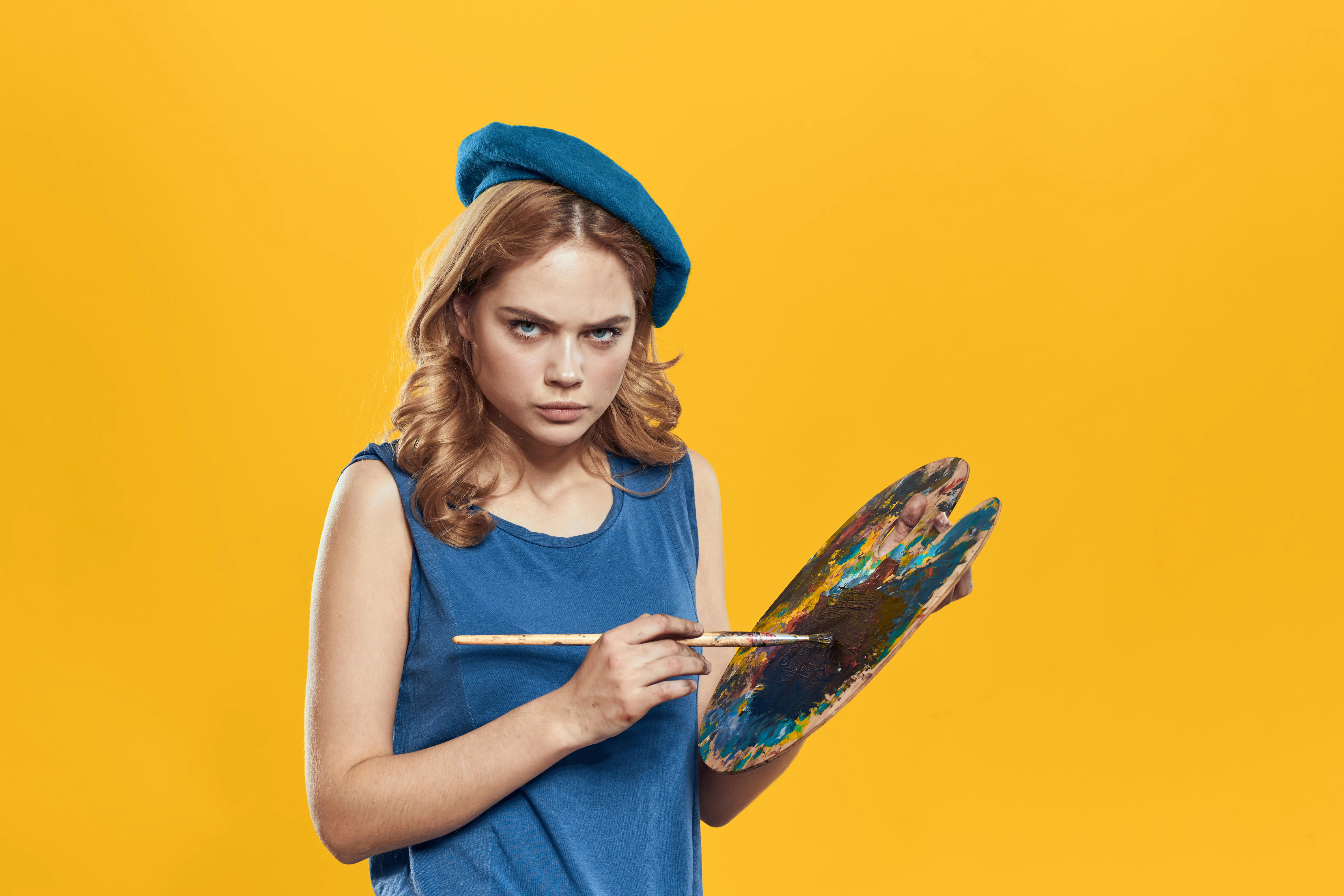 Woman in a beret holding a palette in front of a yellow background